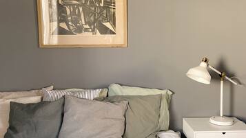 A neatly made bed with a white duvet, a bedside table with a lamp, and a framed abstract artwork on the wall.