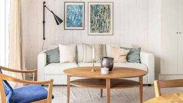 Una sala de estar con un sofá blanco, una mesa de centro redonda de madera y dos cuadros abstractos enmarcados en la pared.