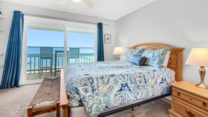 A bedroom with a large bed, a wooden nightstand, a ceiling fan, and a view of the ocean through a sliding glass door. - Boardwalk D6 (Pensacola Beach)