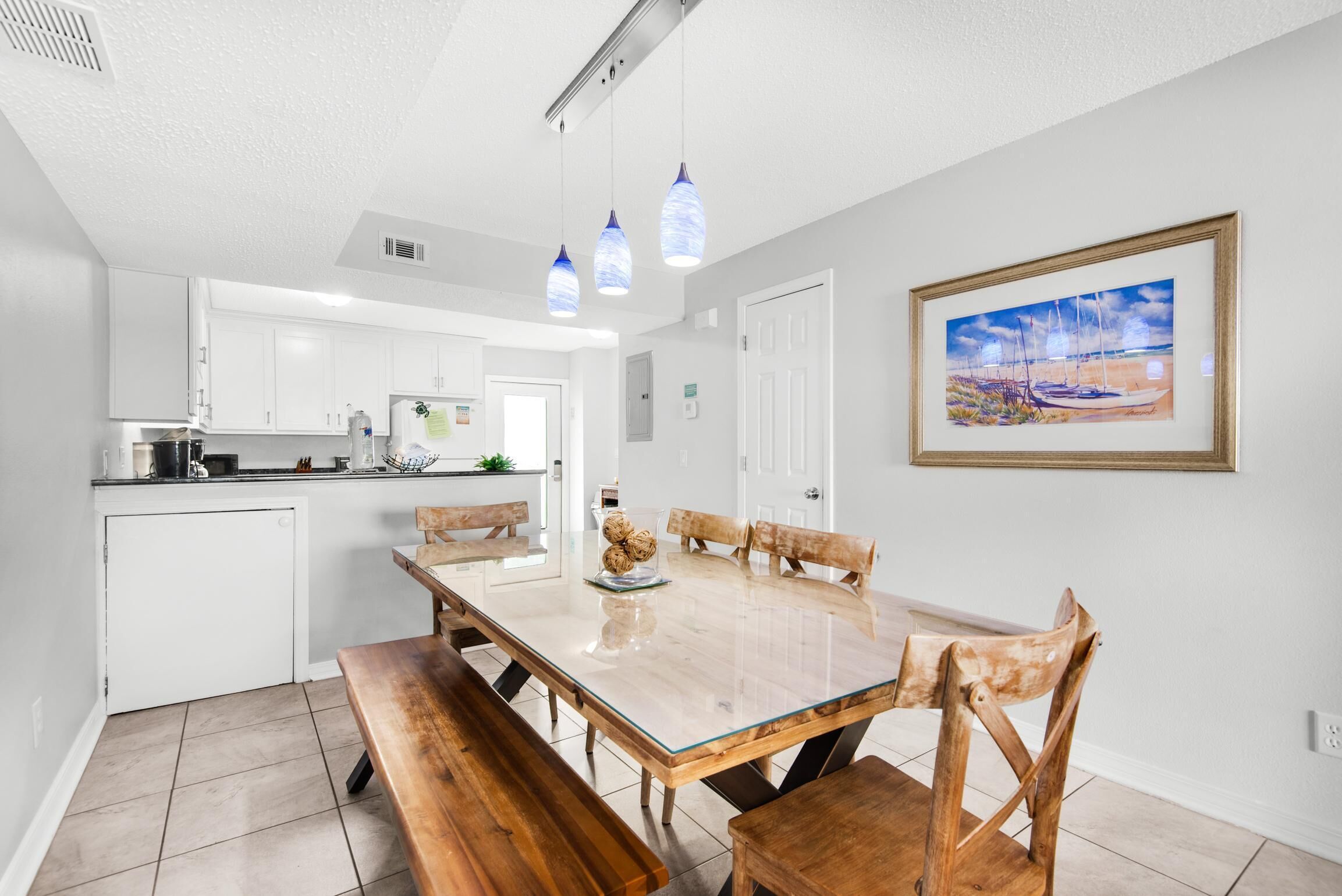 Une cuisine moderne avec des meubles blancs, un coin repas avec une table et des bancs en bois, et un tableau accroché au mur.