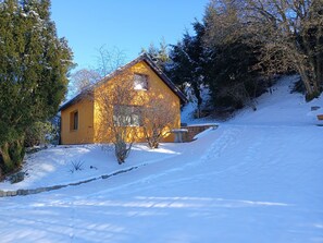 Schneebedeckte Landschaft mit einem gelben Haus und umliegenden Bäumen.
