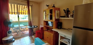 A compact kitchen with a refrigerator, a coffee maker, a wooden cabinet, and a small table.