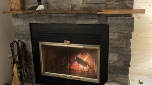 Une cheminée en pierre avec un encadrement noir, une enseigne au-dessus, et un sac à rayures posé sur une plateforme en bois.