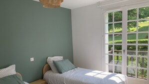 A bedroom with two beds, a large window with a view of a green landscape, and a ceiling light fixture. - Apartment with swimming pool - near train station (Villers-sur-Mer)