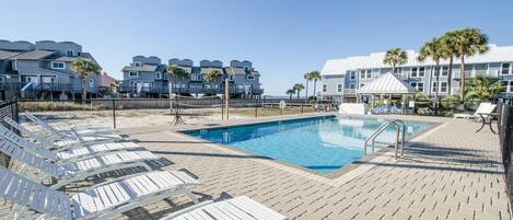 Zona de piscina con sillas de descanso y un edificio con balcones al fondo.