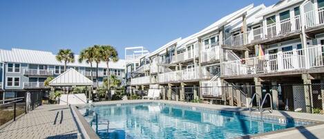 A pool area with a clear blue pool, a covered seating area, and a building with balconies.