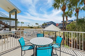 A deck with a round table and chairs, overlooking a beach and residential buildings. - Labahia 123 (Pensacola Beach)