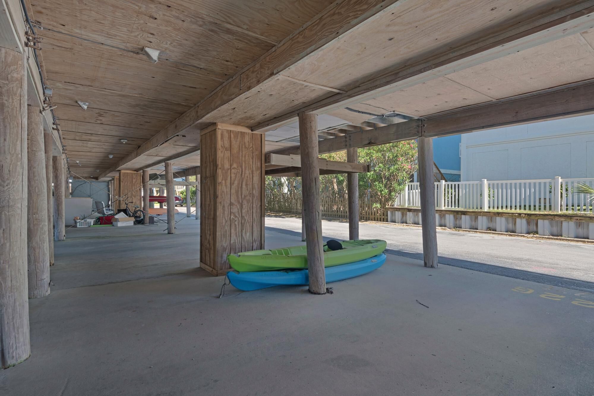 Uma área externa coberta com piso de concreto e pilares de madeira. Dois caiaques estão colocados no chão.