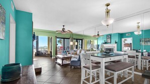 A spacious kitchen with white cabinetry, a dining area with white chairs, and a large window providing a view of the outdoors. - Palm Beach Club 4-127 Parrot-dise Palms (Pensacola Beach)