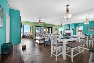 Una cocina amplia con armarios blancos, un comedor con sillas blancas y un gran ventanal que ofrece vistas al exterior.