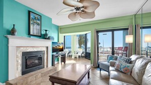 A living room with a fireplace, a ceiling fan, and a view of the outdoors. - Palm Beach Club 4-127 Parrot-dise Palms (Pensacola Beach)