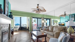 A spacious living room with a fireplace, a large sofa, a coffee table, and a ceiling fan. - Palm Beach Club 4-127 Parrot-dise Palms (Pensacola Beach)