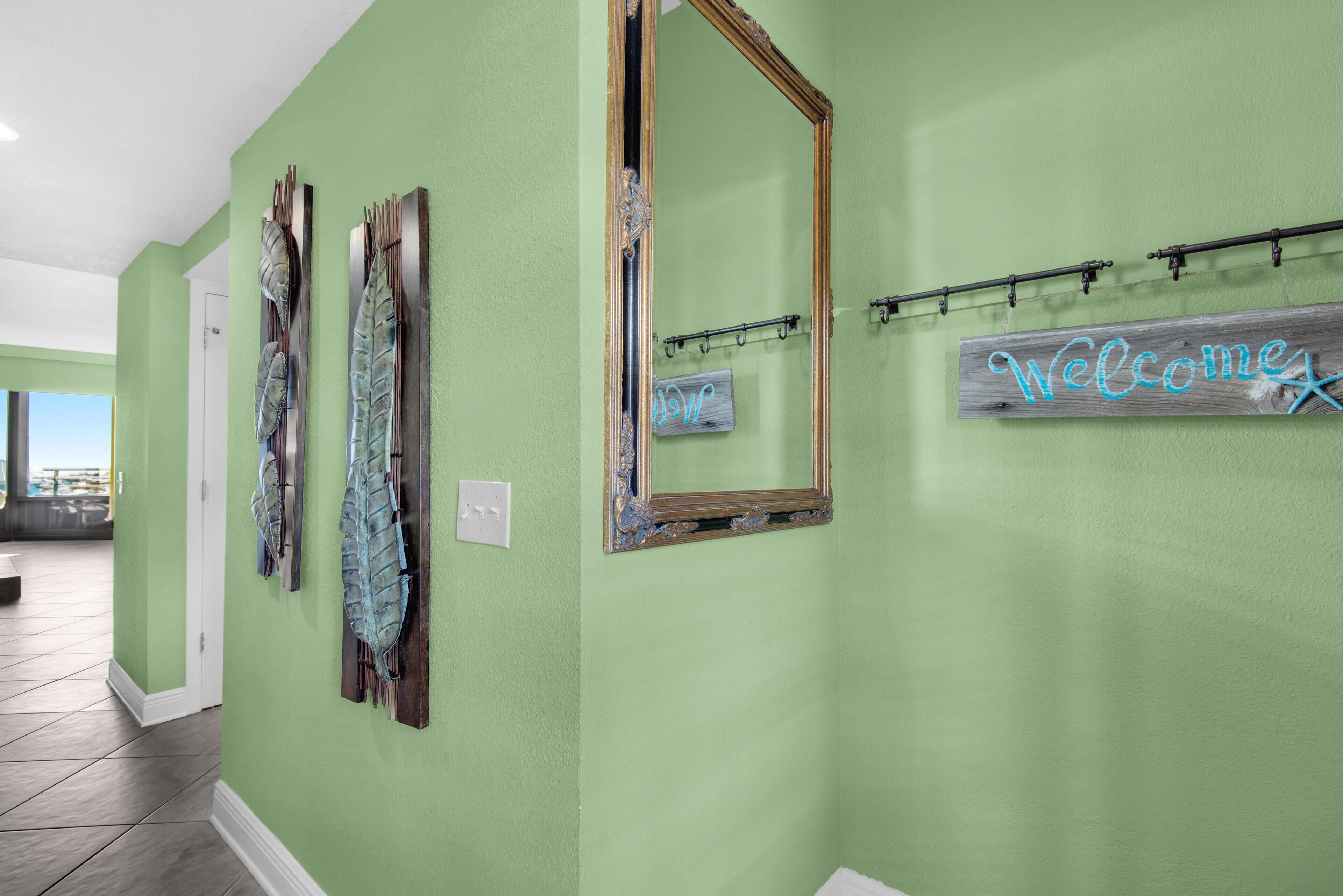 A hallway with green walls, a large mirror, and a 'Welcome' sign.