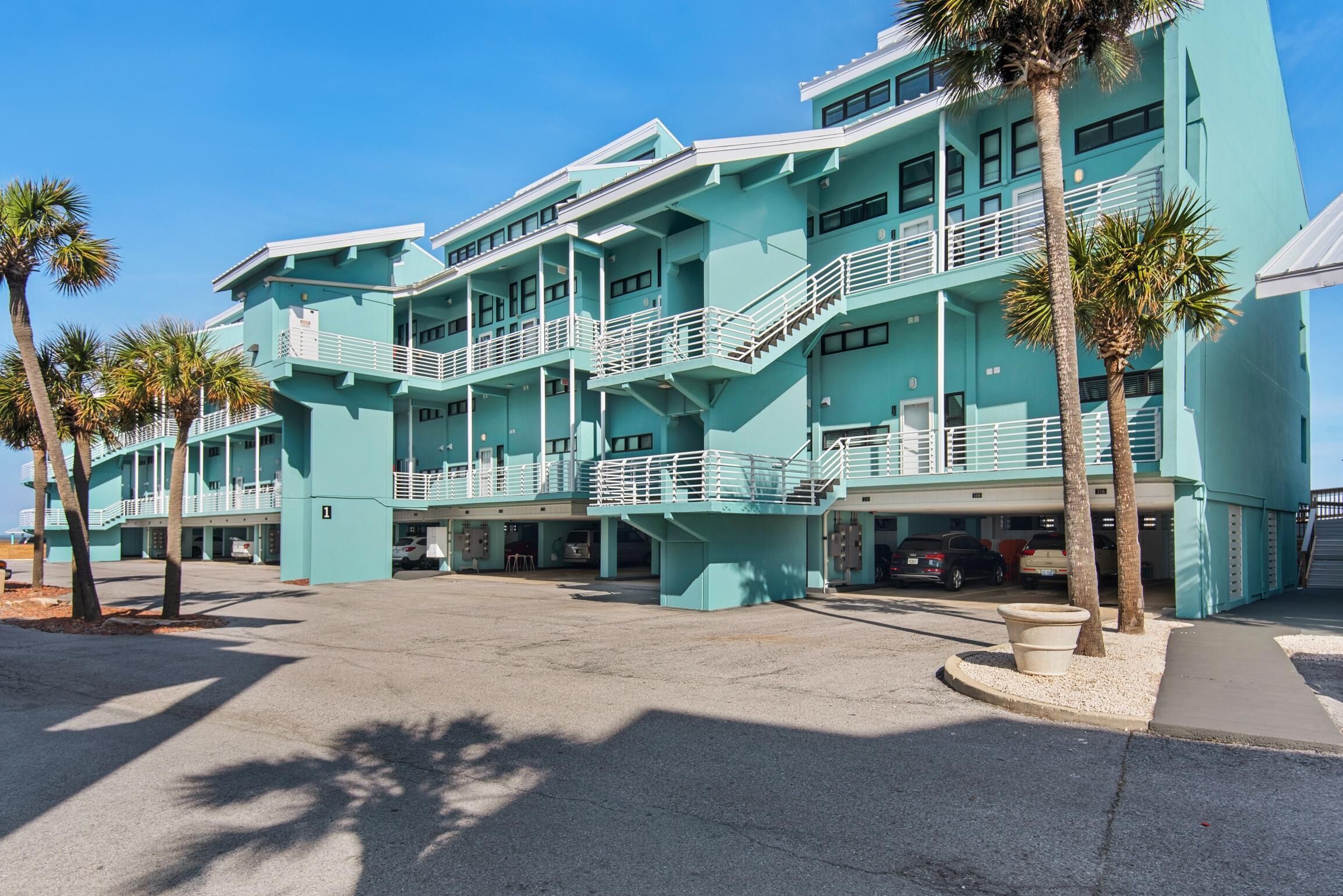 A multi-story hotel with a light blue exterior, multiple balconies, and a parking area.