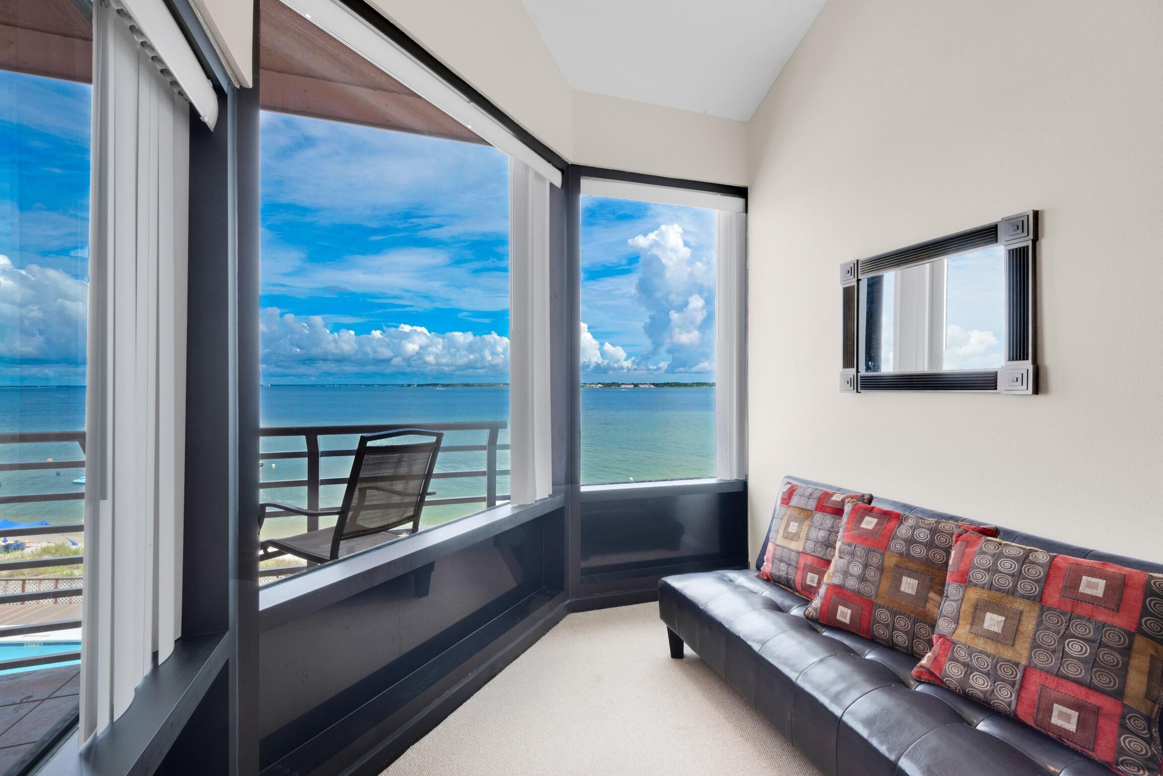 A balcony with a view of the sea, a sofa with patterned cushions, and a framed mirror on the wall.