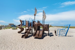 A playground with slides and climbing structures on a sandy beach. - Palm Beach Club 2-219 (Pensacola Beach)