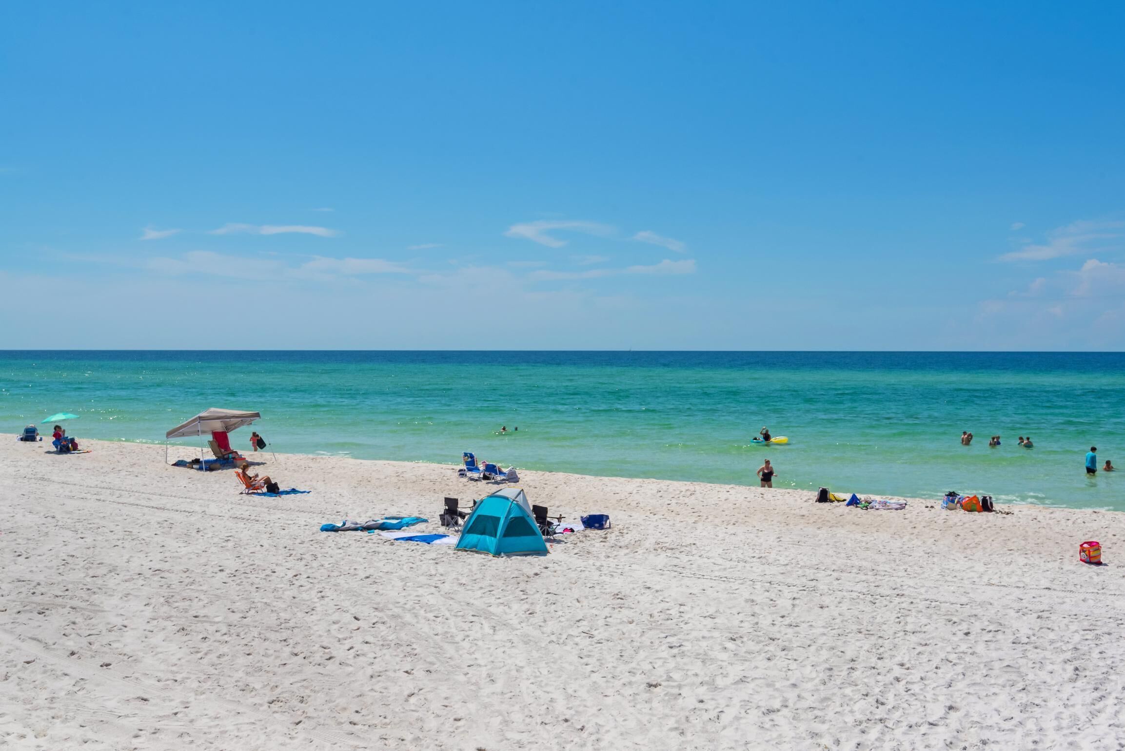 A beach with tents, umbrellas, and people swimming.