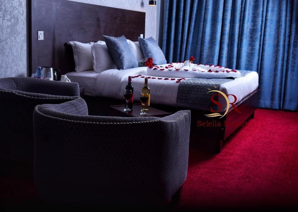 Ein Hotelzimmer mit einem Bett, zwei Sesseln, einem roten Teppich und einer Minibar.