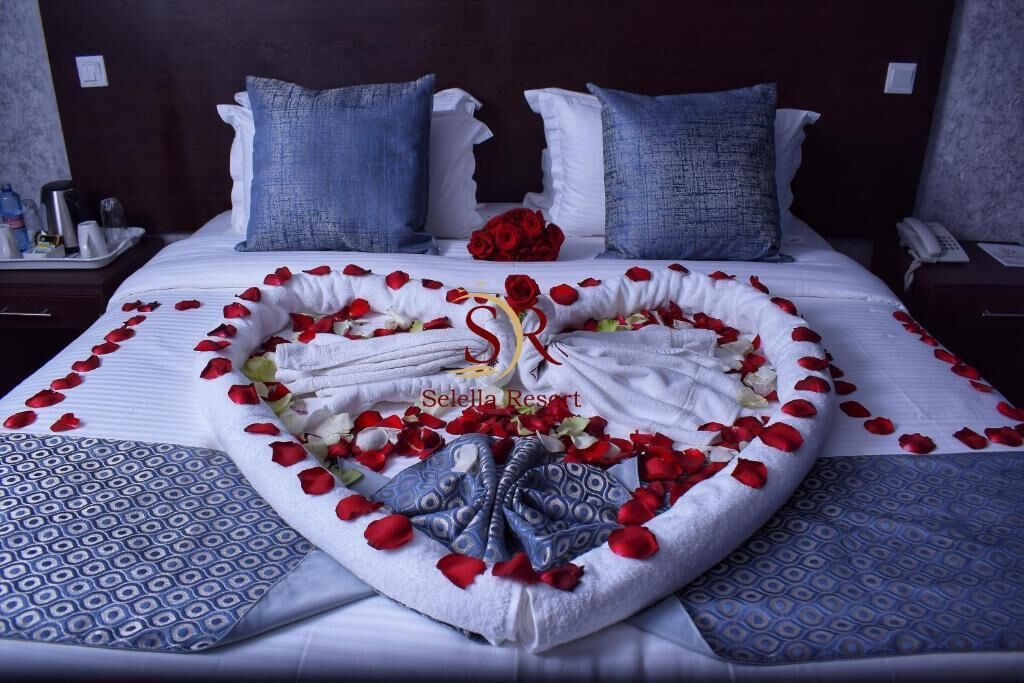 Ein Bett mit Rosenblättern und Handtüchern, die in Herzform drapiert sind, ein Rosenstrauß aus roten Rosen und ein dekorativer Schwan.