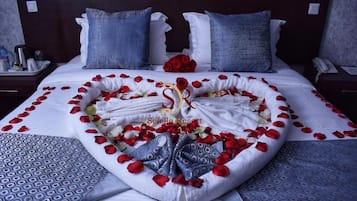 A bed with rose petals and towels arranged in a heart shape, a bouquet of red roses, and a decorative swan.