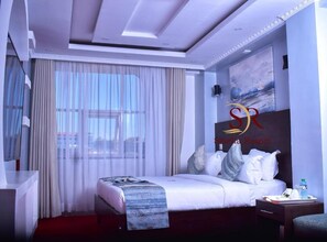 A modern hotel room with a large bed, a desk, and a painting on the wall. - Selella Resort (Kisumu)