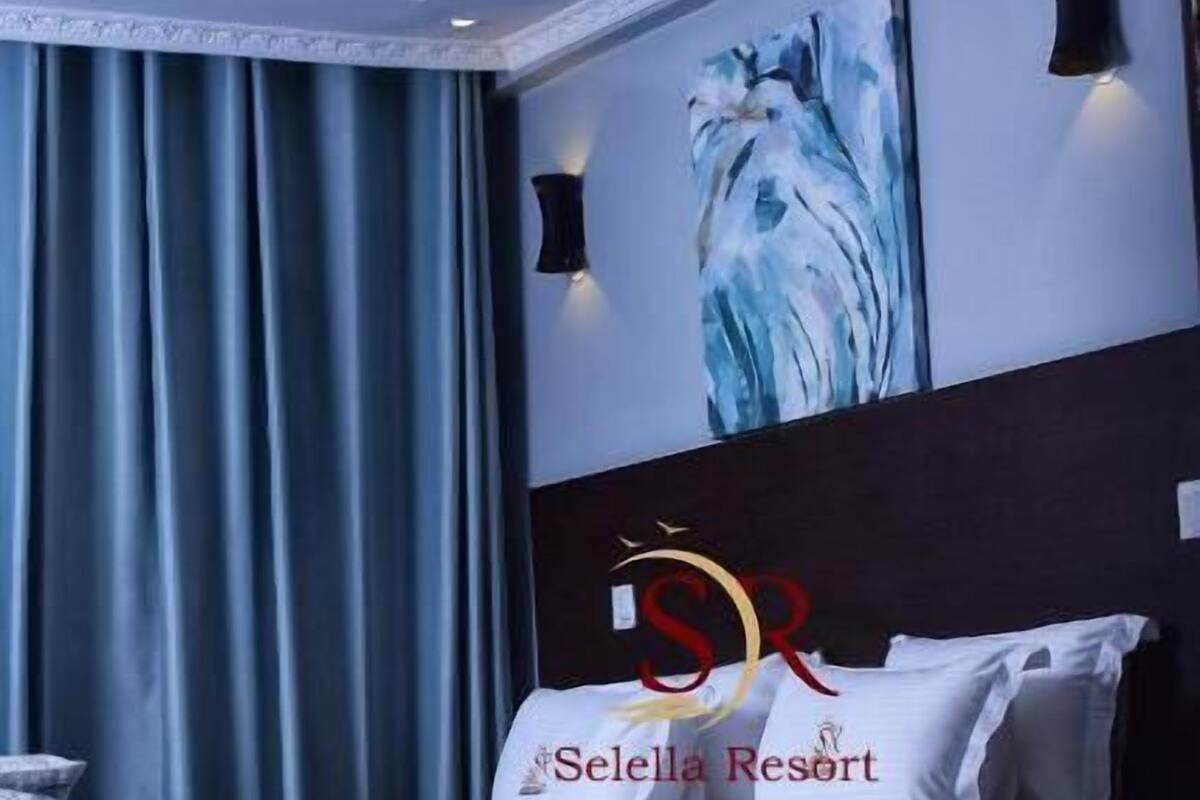 A modern bedroom with a large bed, a painting on the wall, and a ceiling light fixture.