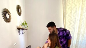 A room with a wooden table, a laptop, a white mug, and a small shelf with a plant. - Barco Verde Hostel  (Isla Holbox)