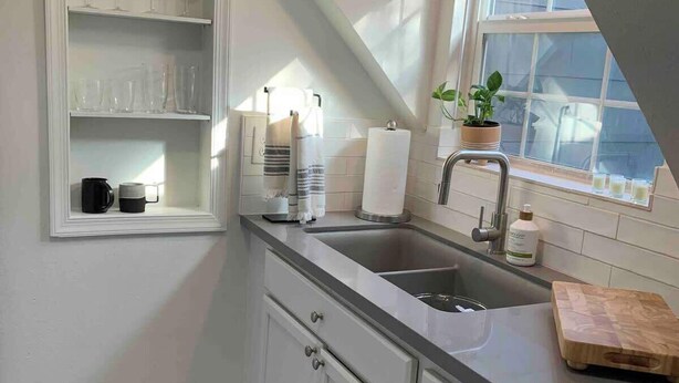 Een moderne keuken met witte kasten, een ingebouwde wijnrek, een groot raam met uitzicht, en een houten snijplank op het aanrecht.