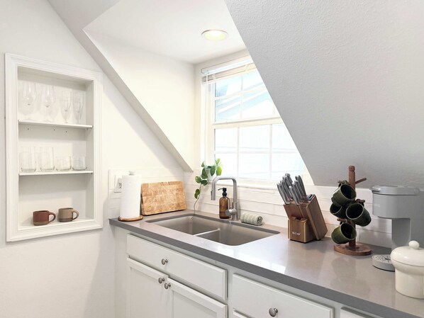 A kitchen with a built-in sink, a window, and a shelf with glassware.