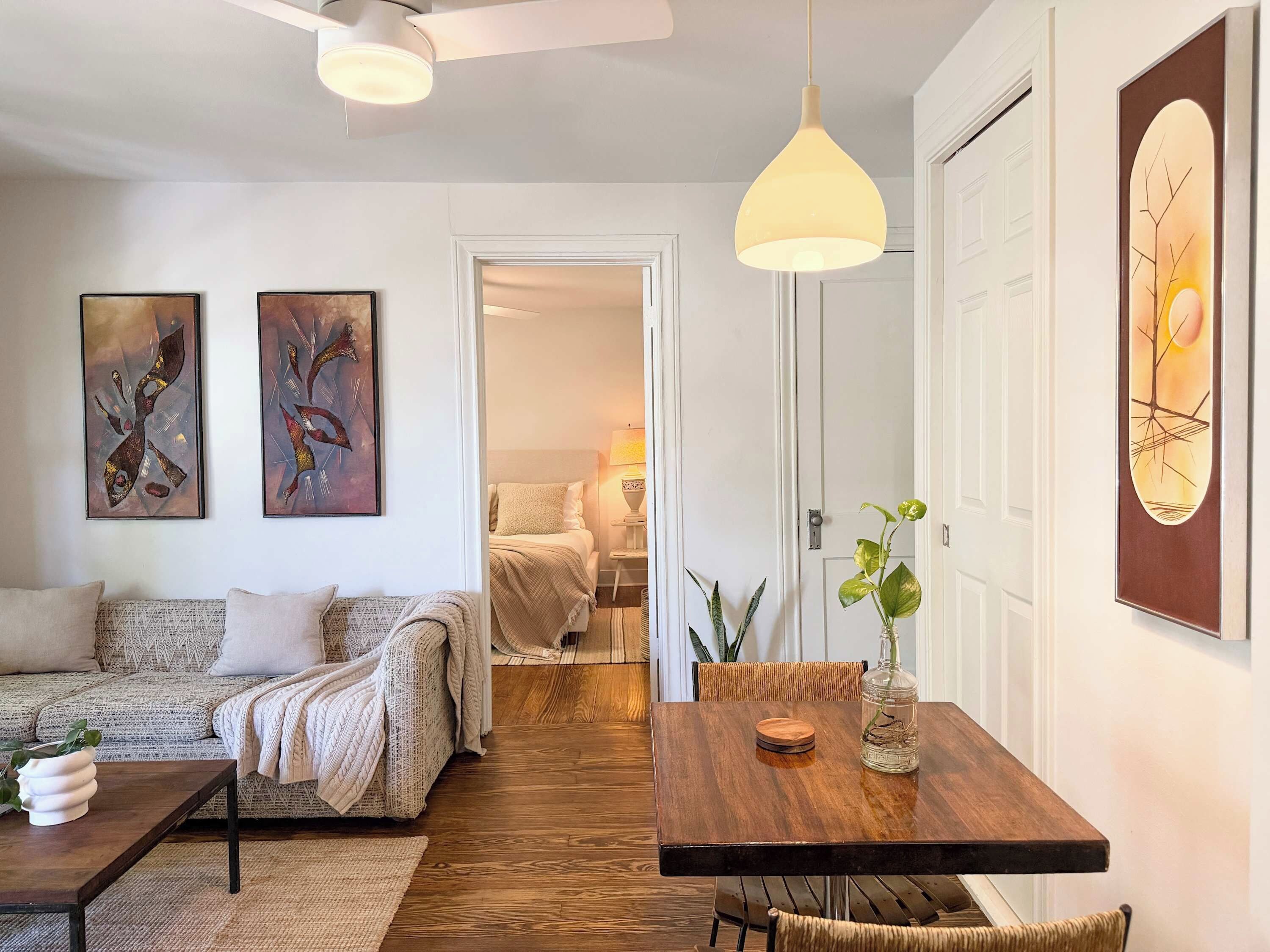A modern living room with a sofa, a dining table with chairs, and artwork on the walls.