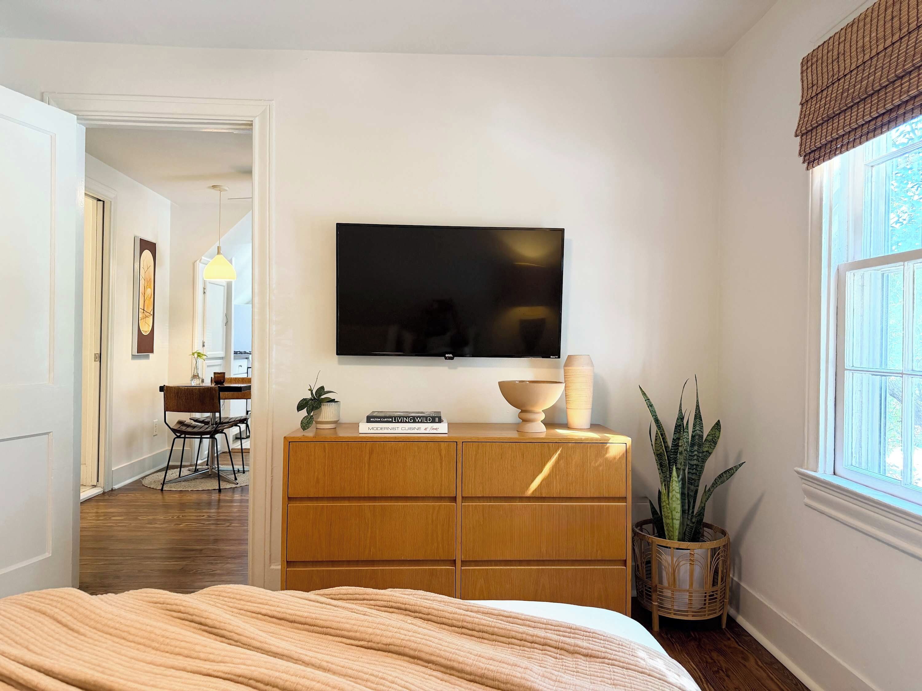 Un dormitorio con una cama, un aparador de madera, un televisor y un ventanal con vistas.