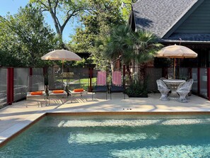 A poolside area with a table and chairs, umbrellas, and a fenced patio.