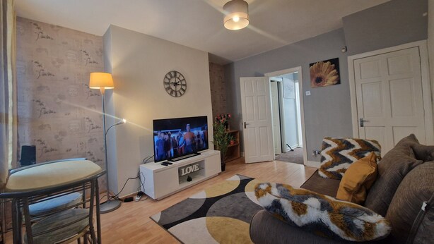 Ett vardagsrum med en tv, en soffa, en fåtölj, en lampa och en klocka på väggen.