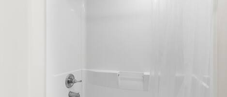 Un baño moderno con ducha, bañera con mampara de vidrio y pared de azulejos blancos.