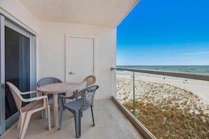 Uma varanda com mesa e cadeiras, uma porta e vista para a praia.