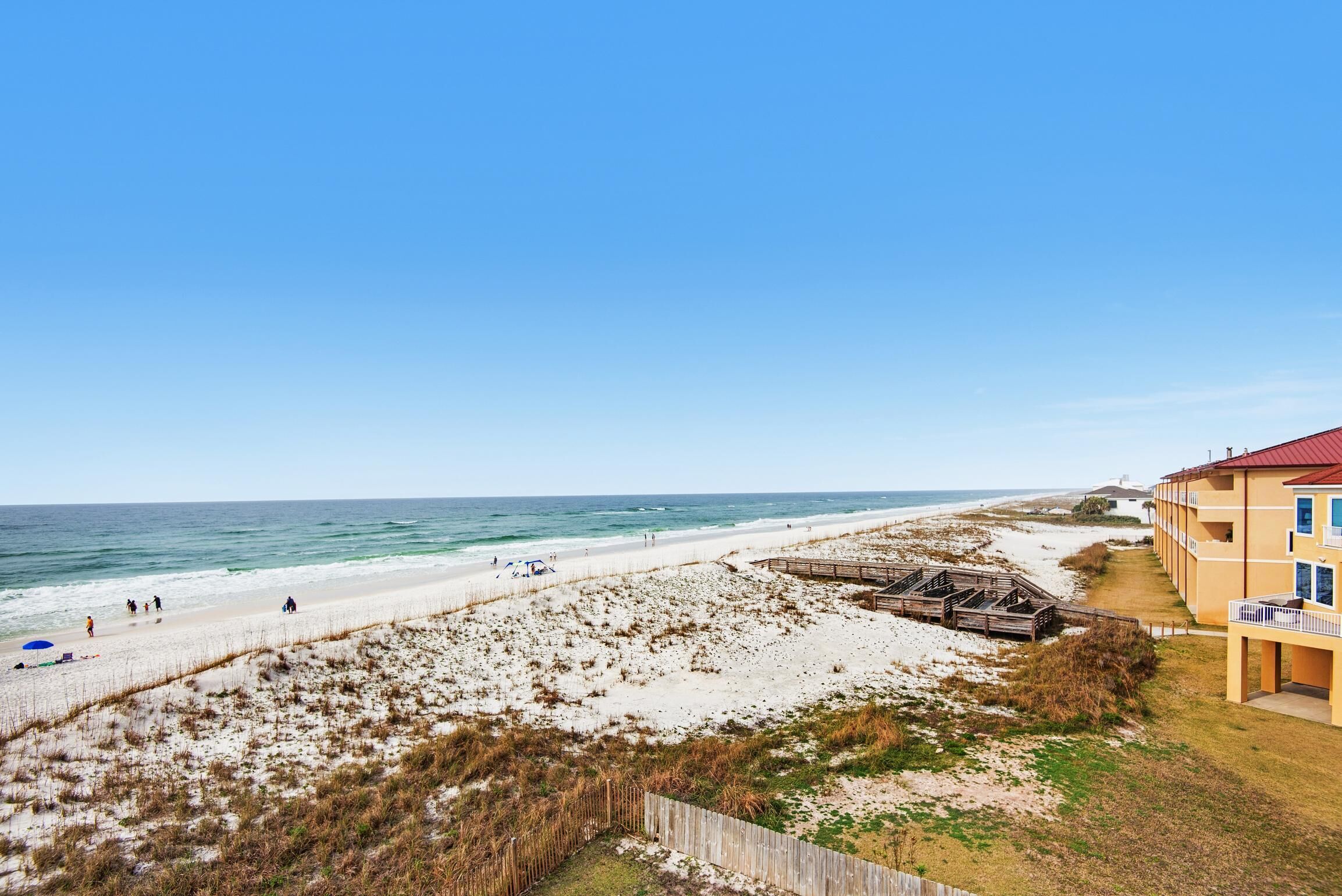 En strand med utsikt, en träpromenad som leder ner till stranden, en sandstrand och en byggnad med ett rött tak.