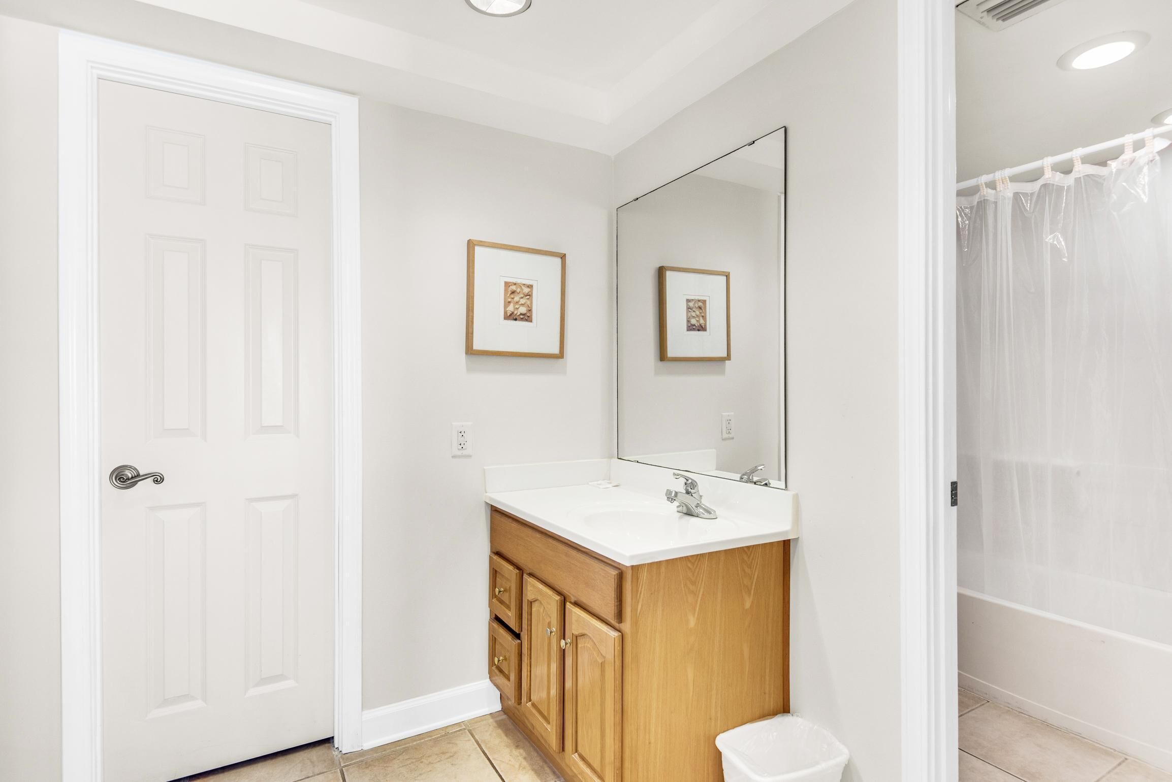Une salle de bain avec une porte blanche, des meubles en bois, un grand miroir et un rideau de douche.