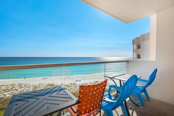 A balcony with a table and chairs overlooking a beach.
