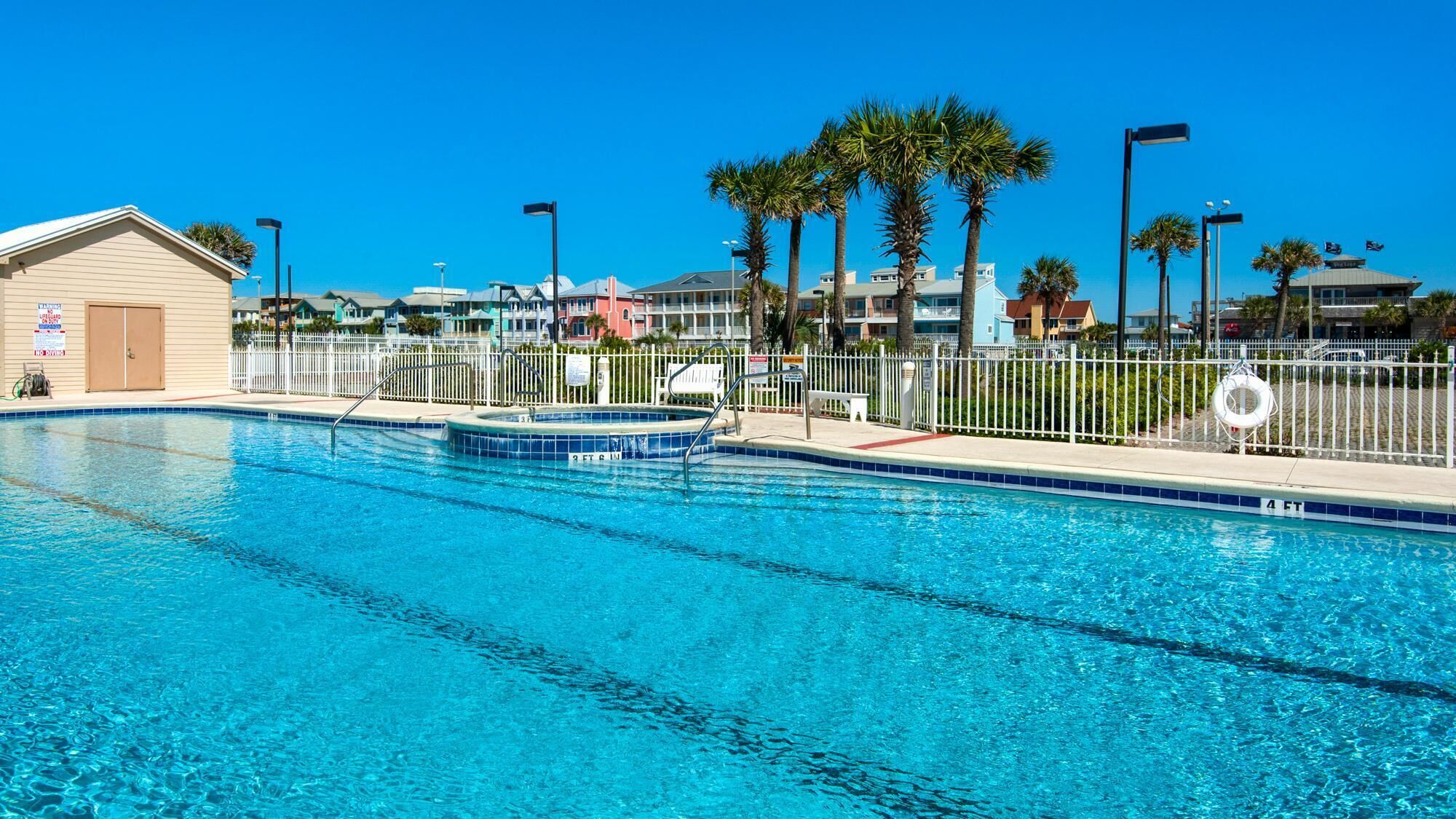 A clear blue swimming pool with a lifeguard tower, palm trees, and a white fence.