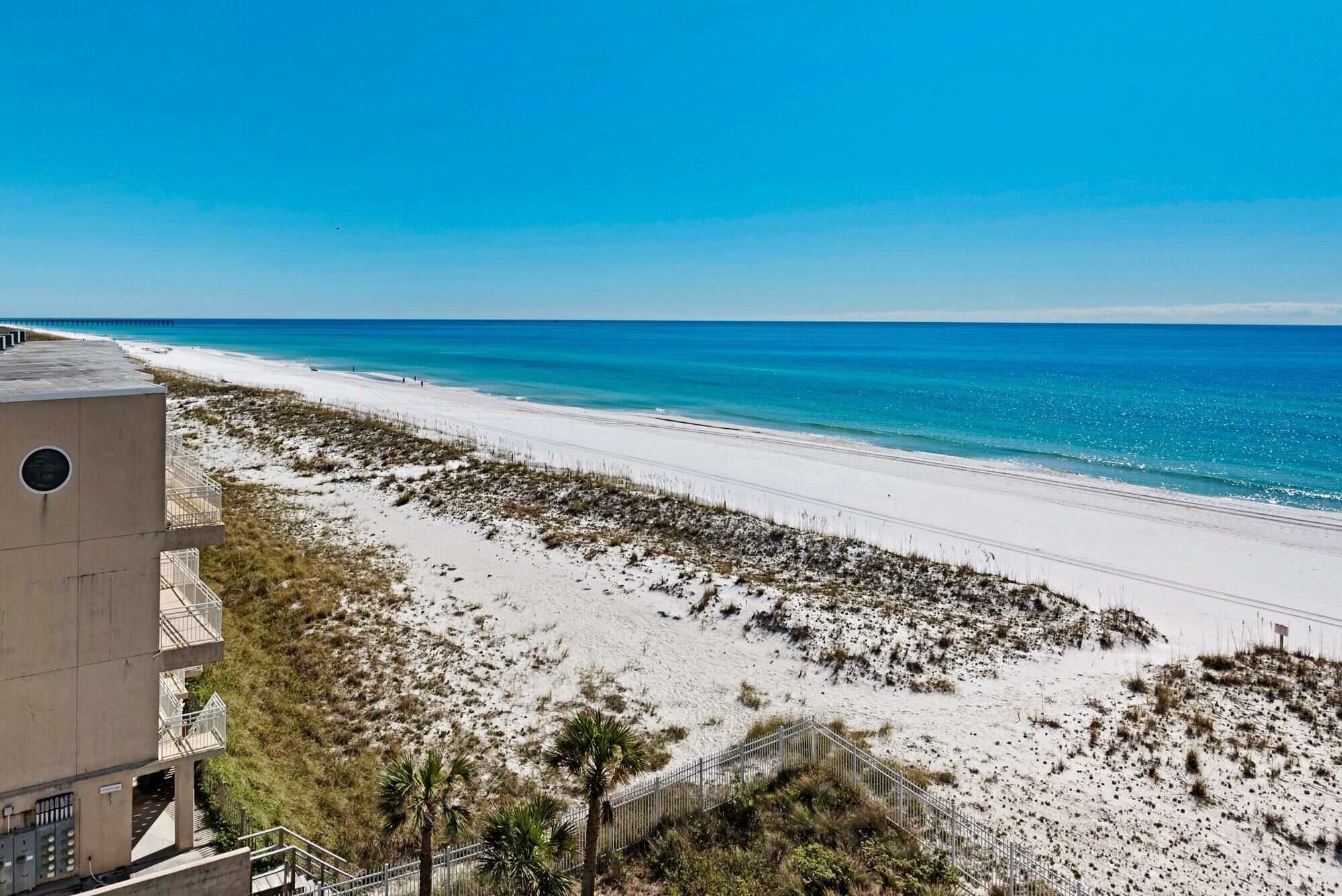 Ein Strand mit freiem Blick auf das Meer, ein sandiger Pfad, der zum Strand führt, und ein Gebäude mit Balkonen, das den Strand überblickt.