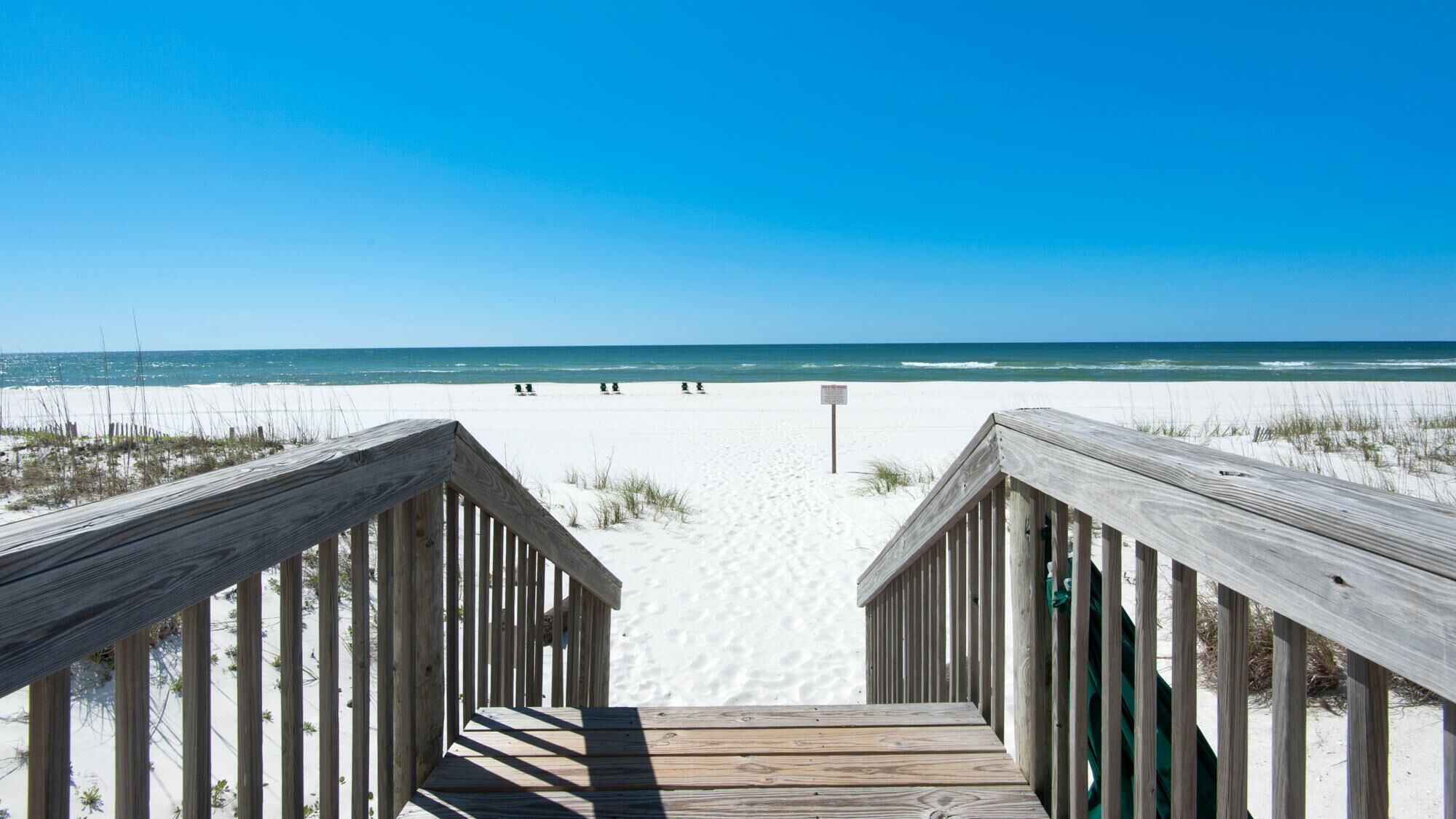 A wooden boardwalk leading to a beach with white sand and a clear blue sky.