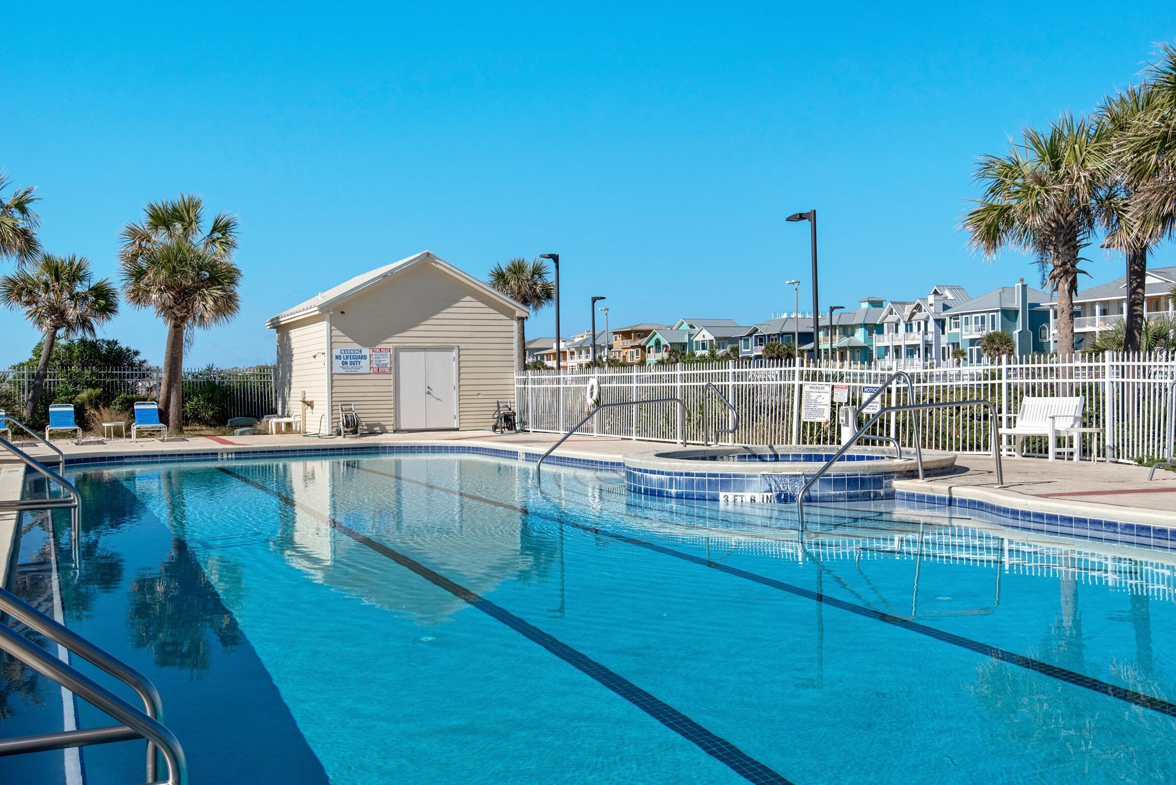 A swimming pool with clear blue water, surrounded by a white fence and palm trees.