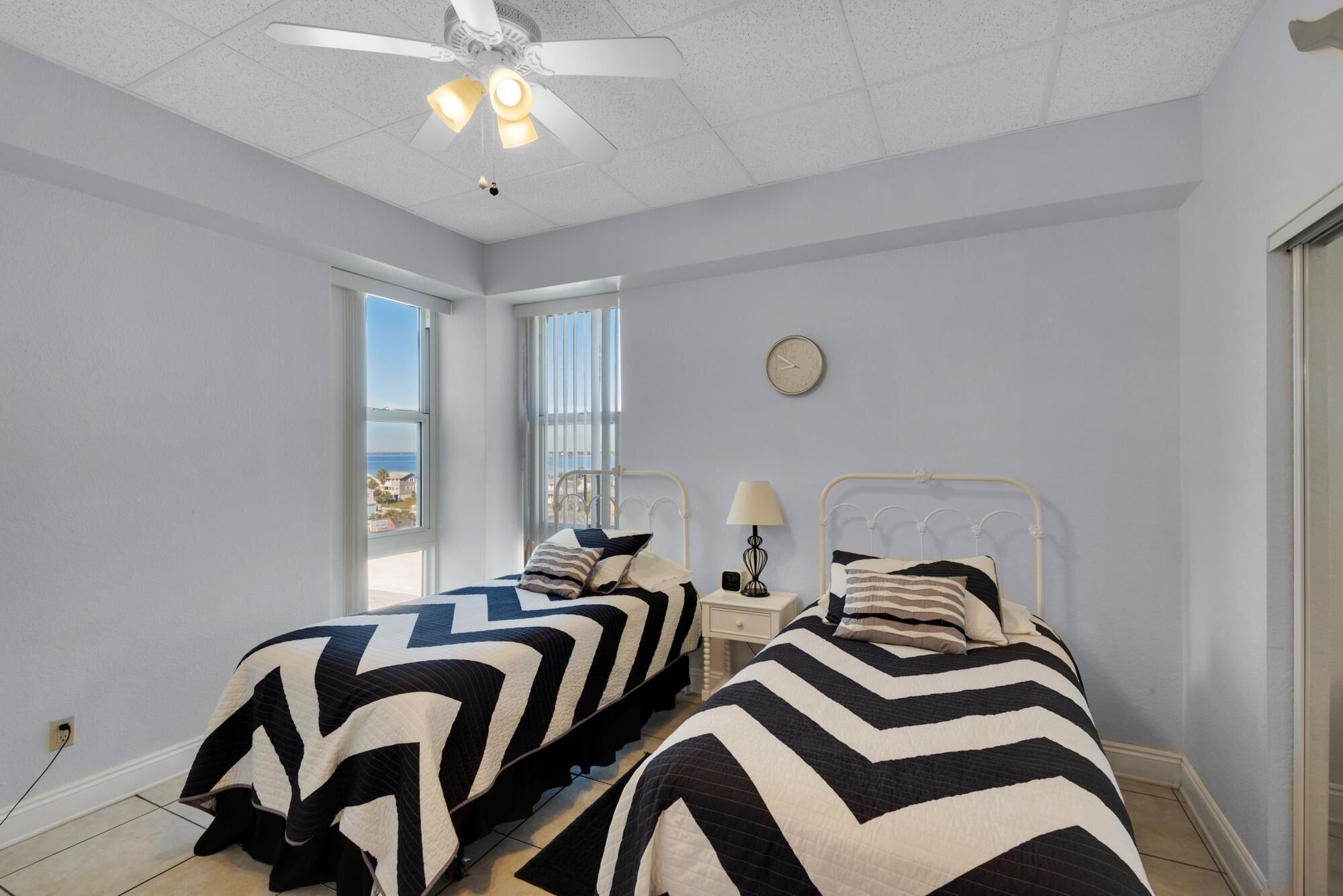 A bedroom with two beds, a ceiling fan, a clock, and a window with a view.