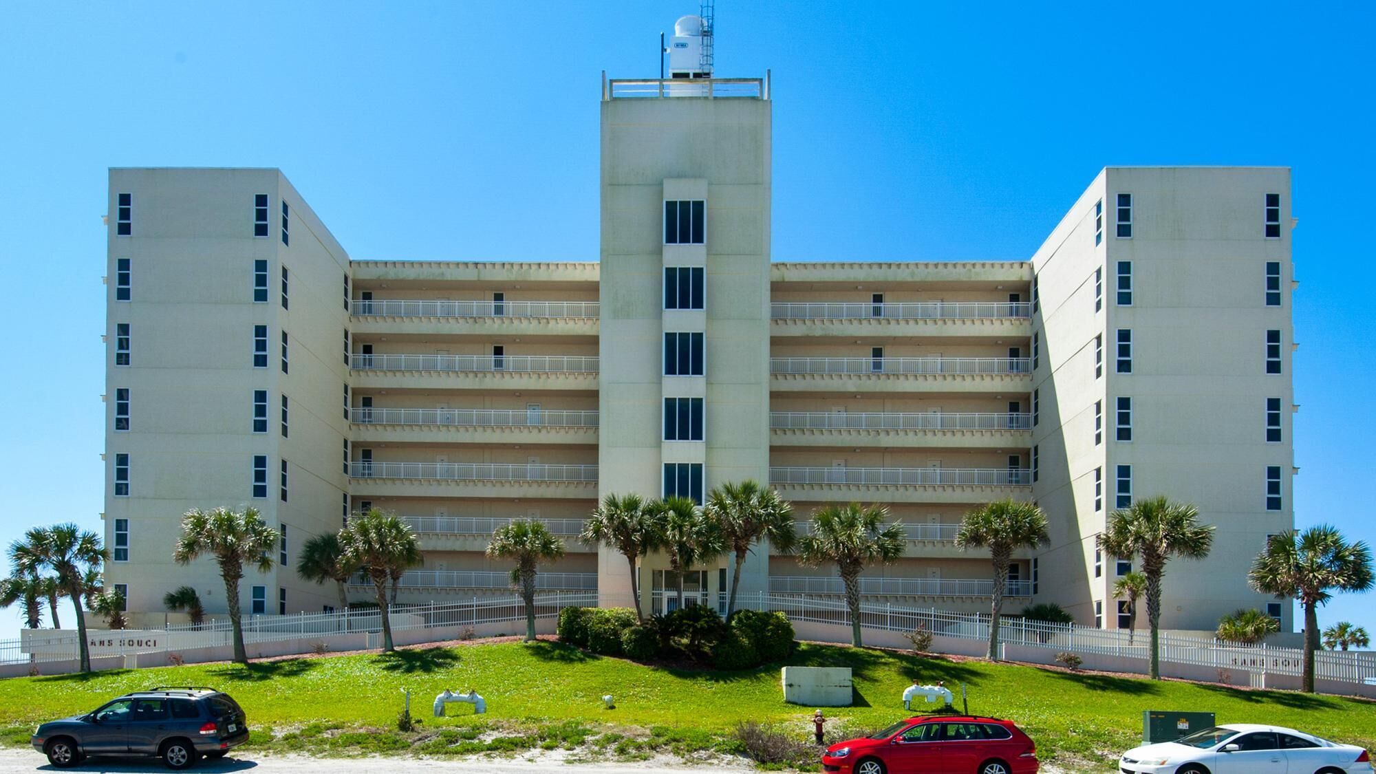 A multi-story hotel with a central tower, balconies on each floor, and palm trees in the foreground.