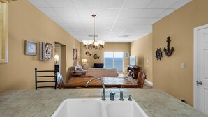 A kitchen with a double sink, a dining area with a wooden table, and a living room with a sofa and a chandelier.