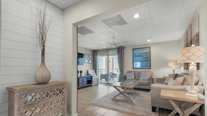 A spacious living room with a large window, a sofa, a coffee table, and a decorative vase. - Sans Souci Unit 601 (Pensacola Beach)