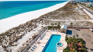 An aerial view of a beachside resort with a swimming pool, lounge chairs, and a small building. - Sans Souci Unit 601 (Pensacola Beach)