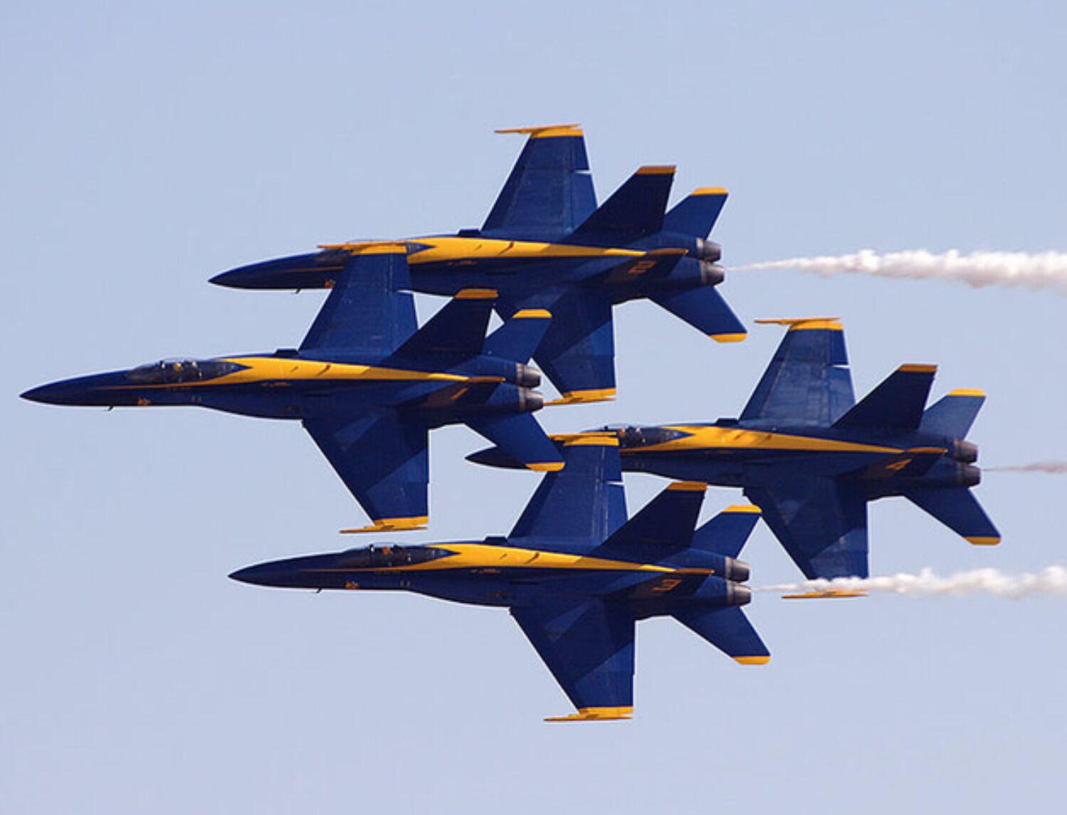 Four blue and yellow aircraft flying in formation with smoke trails.