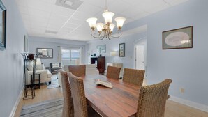 A dining area with a wooden table, wicker chairs, and a chandelier. - Sans Souci Unit 705 (Pensacola Beach)