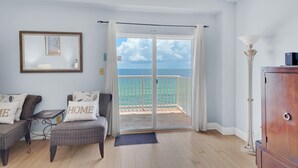 A room with a view of the sea, a balcony with a white railing, a sofa with 'HOME' pillows, a framed picture on the wall, and a tall floor lamp. - Sans Souci Unit 705 (Pensacola Beach)